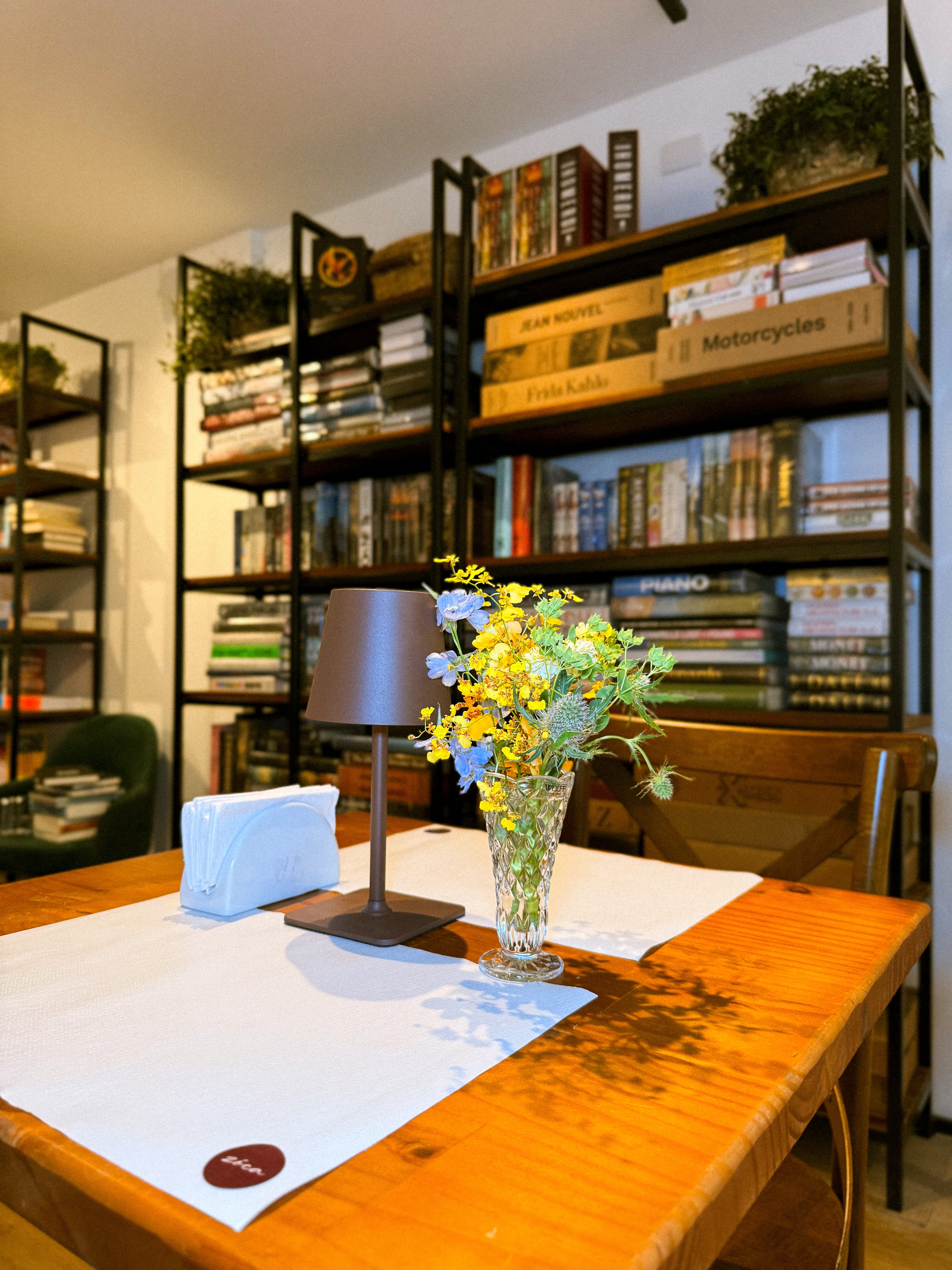 Interior do Zóca — mesas de madeira, estantes de livros e flores no Real Parque