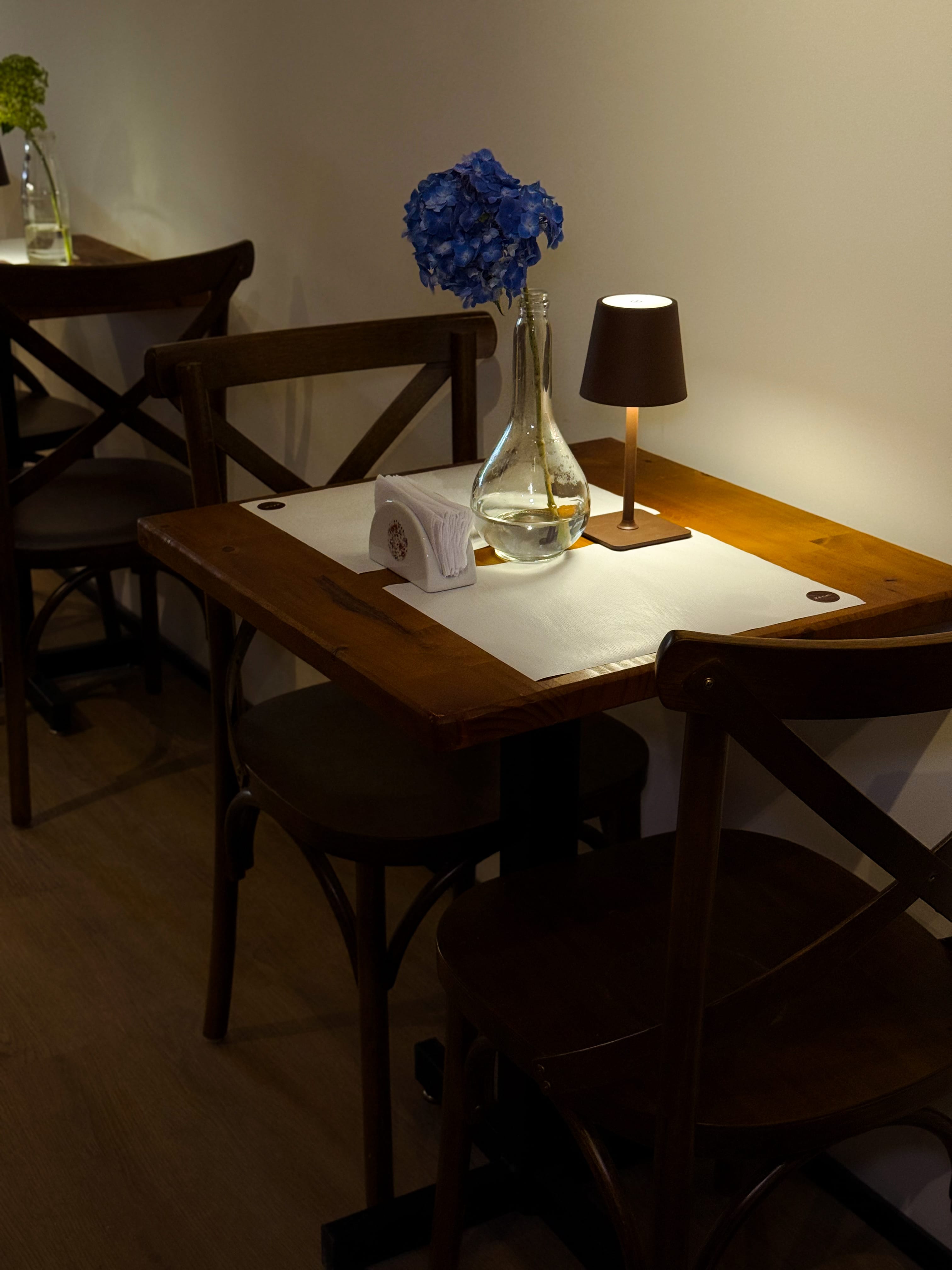 Mesa íntima com flores azuis e luminária no Zóca — ambiente aconchegante